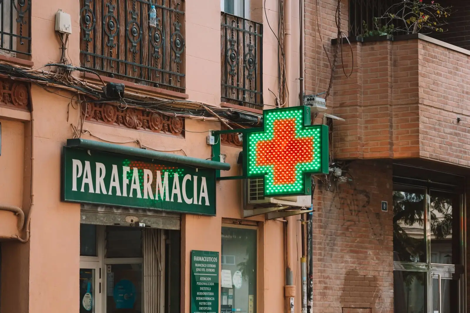 Croix verte lumineuse et enseigne d'une parapharmacie sur une façade de brique