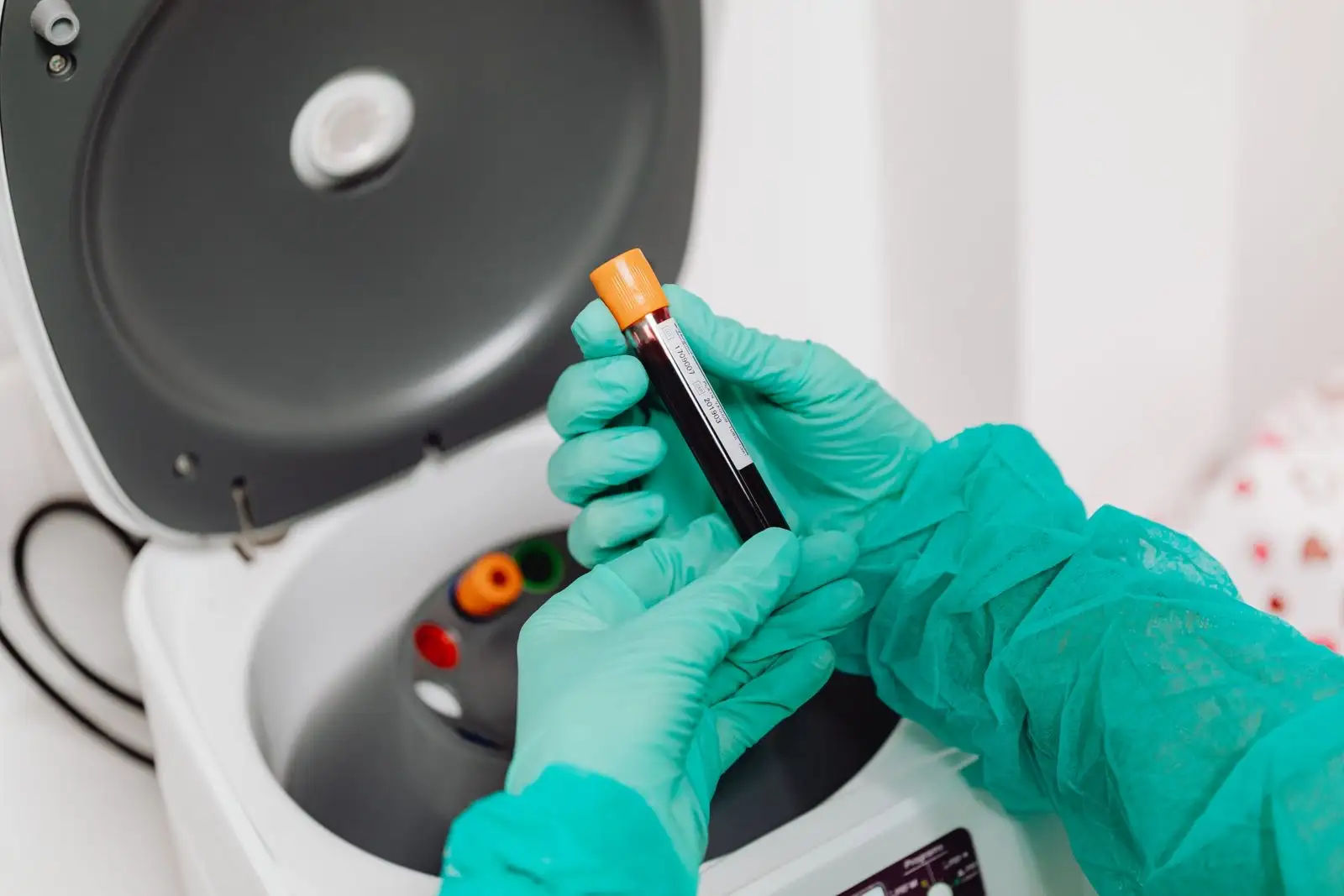 Mains gantées plaçant un tube de sang dans une centrifugeuse de laboratoire, avant un bilan hépatique