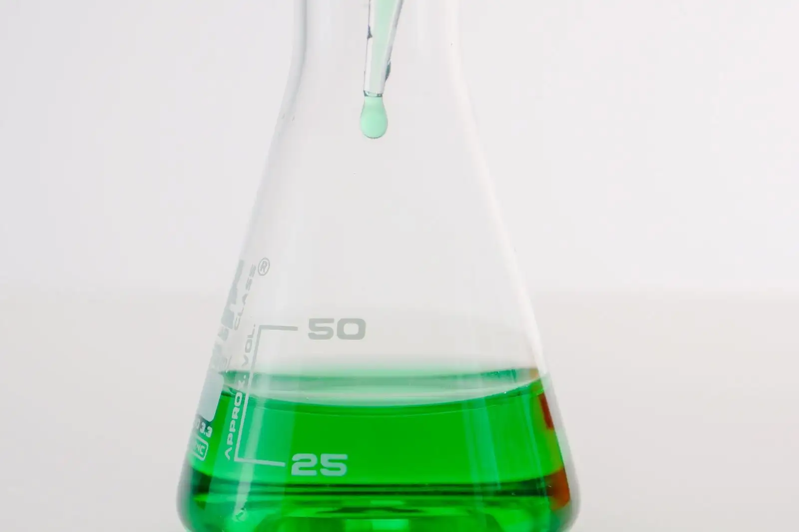 Pipette déposant une goutte dans une fiole de laboratoire graduée contenant un liquide vert