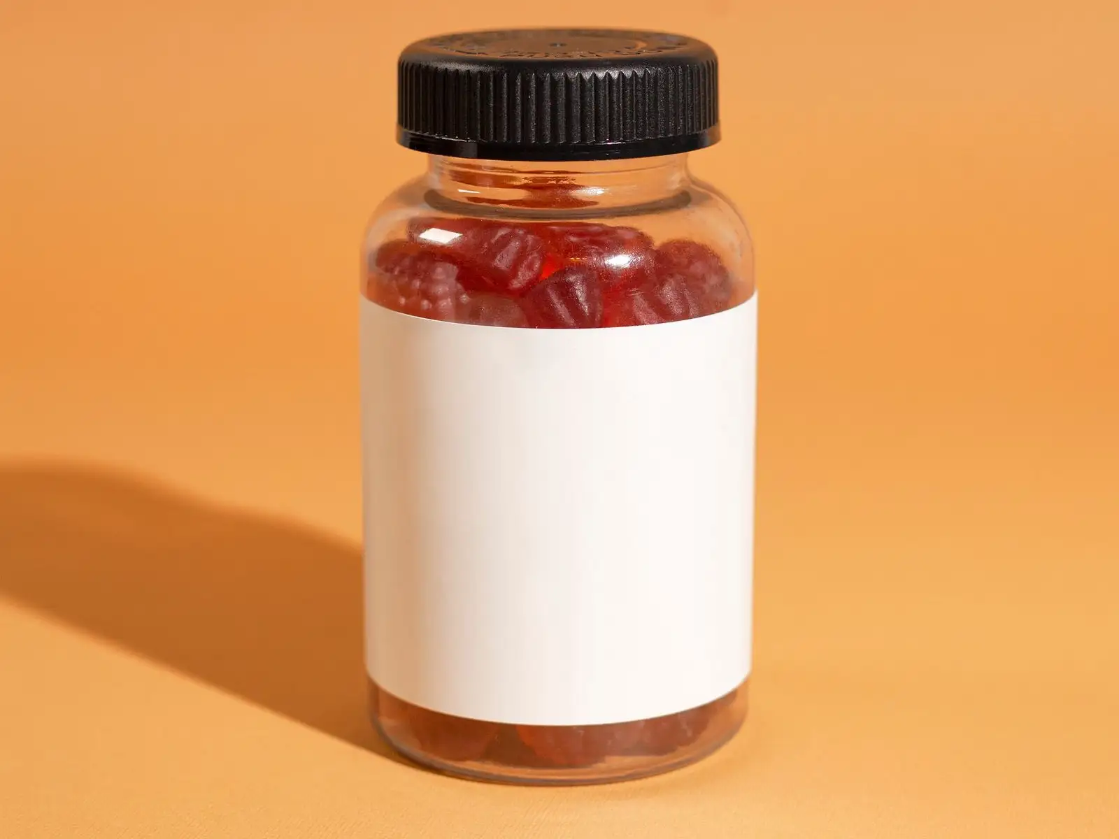 Pilulier transparent rempli de gommes rouges, étiquette vierge, sur fond orange
