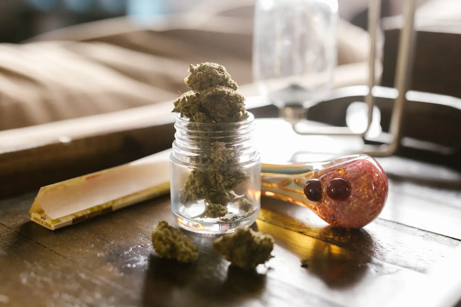 Petit bocal en verre rempli de têtes de chanvre séchées, posé sur une table en bois à côté d'un carnet de feuilles à rouler
