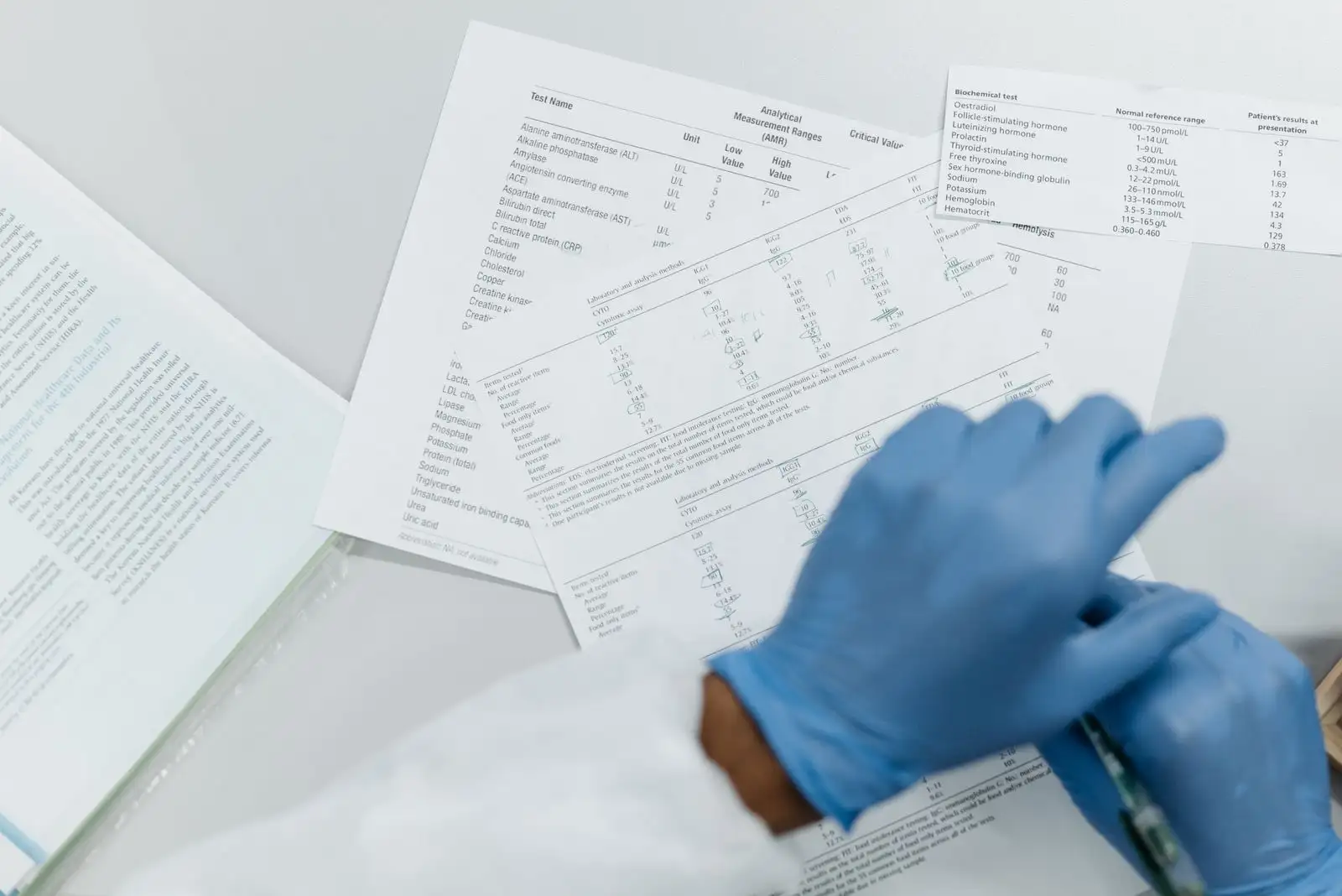 Mains gantées relisant des résultats d'analyse de laboratoire imprimés, tableaux de valeurs sur une table blanche