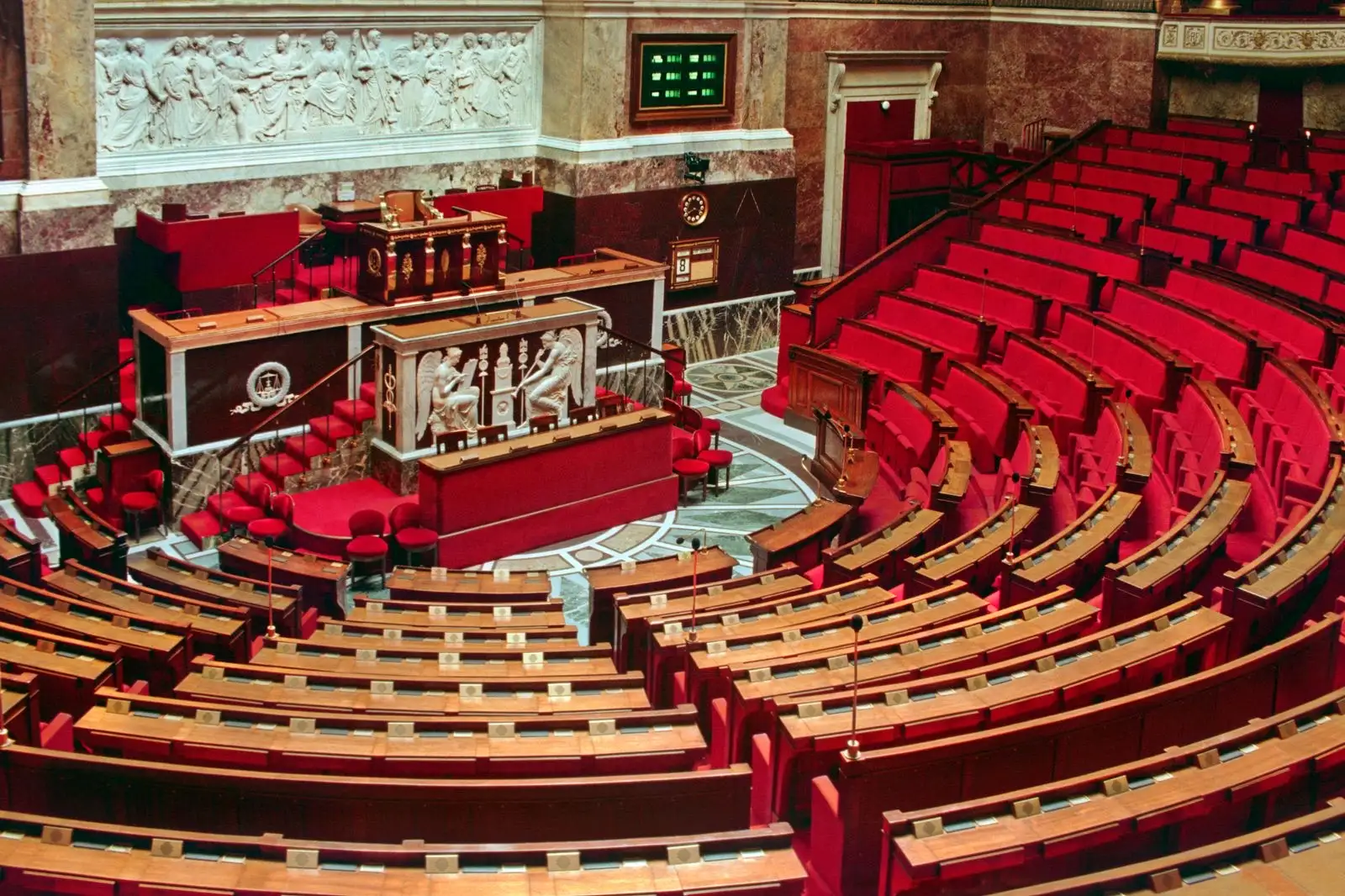 Hémicycle vide de l'Assemblée nationale, rangées de sièges rouges face à la tribune