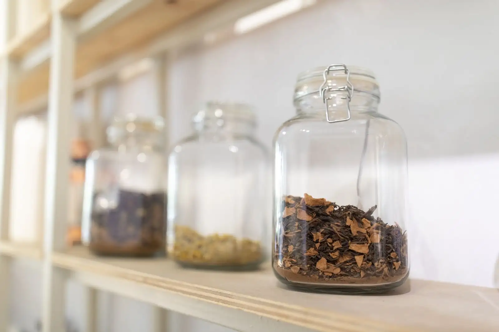 Bocaux en verre remplis de plantes séchées alignés sur une étagère en bois