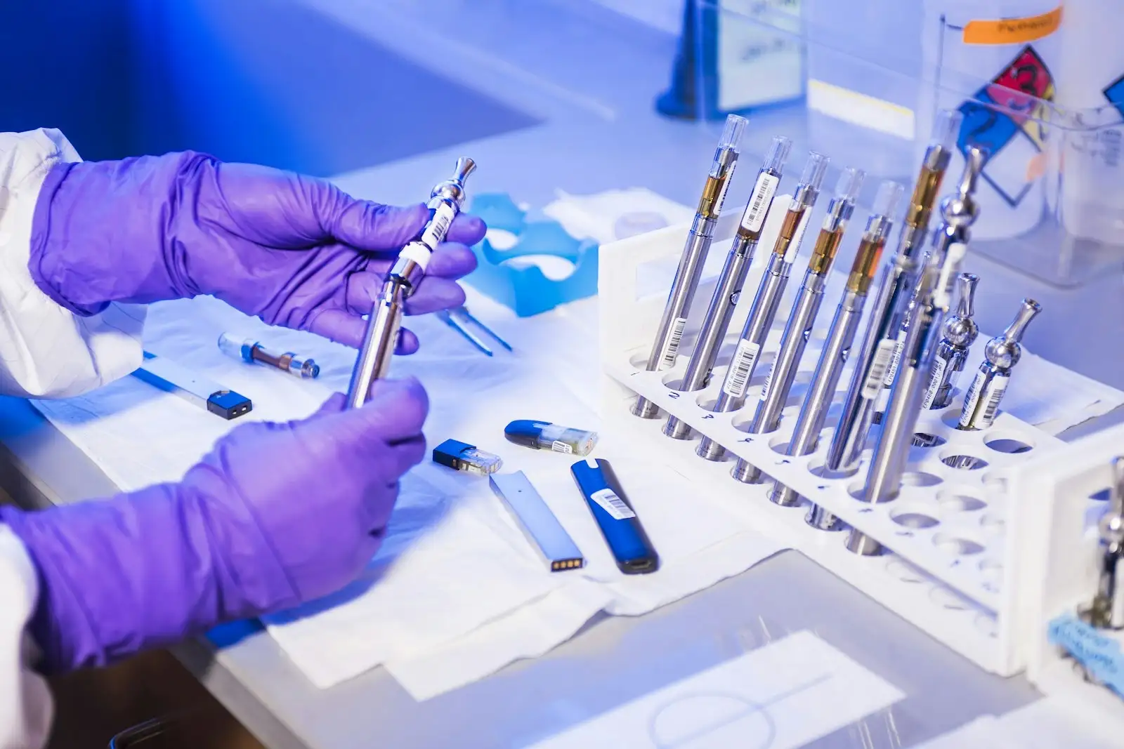 Mains gantées examinant des cigarettes électroniques dans un laboratoire d'analyse, là où l'on identifie les cannabinoïdes de synthèse