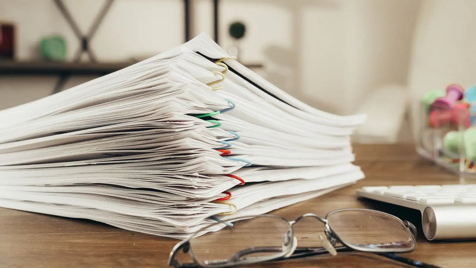 Pile de documents agrafés sur un bureau, à côté d'une paire de lunettes