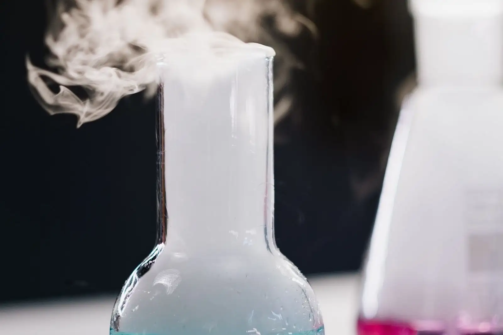 Ballon de laboratoire d'où s'échappe une vapeur blanche, sur fond sombre