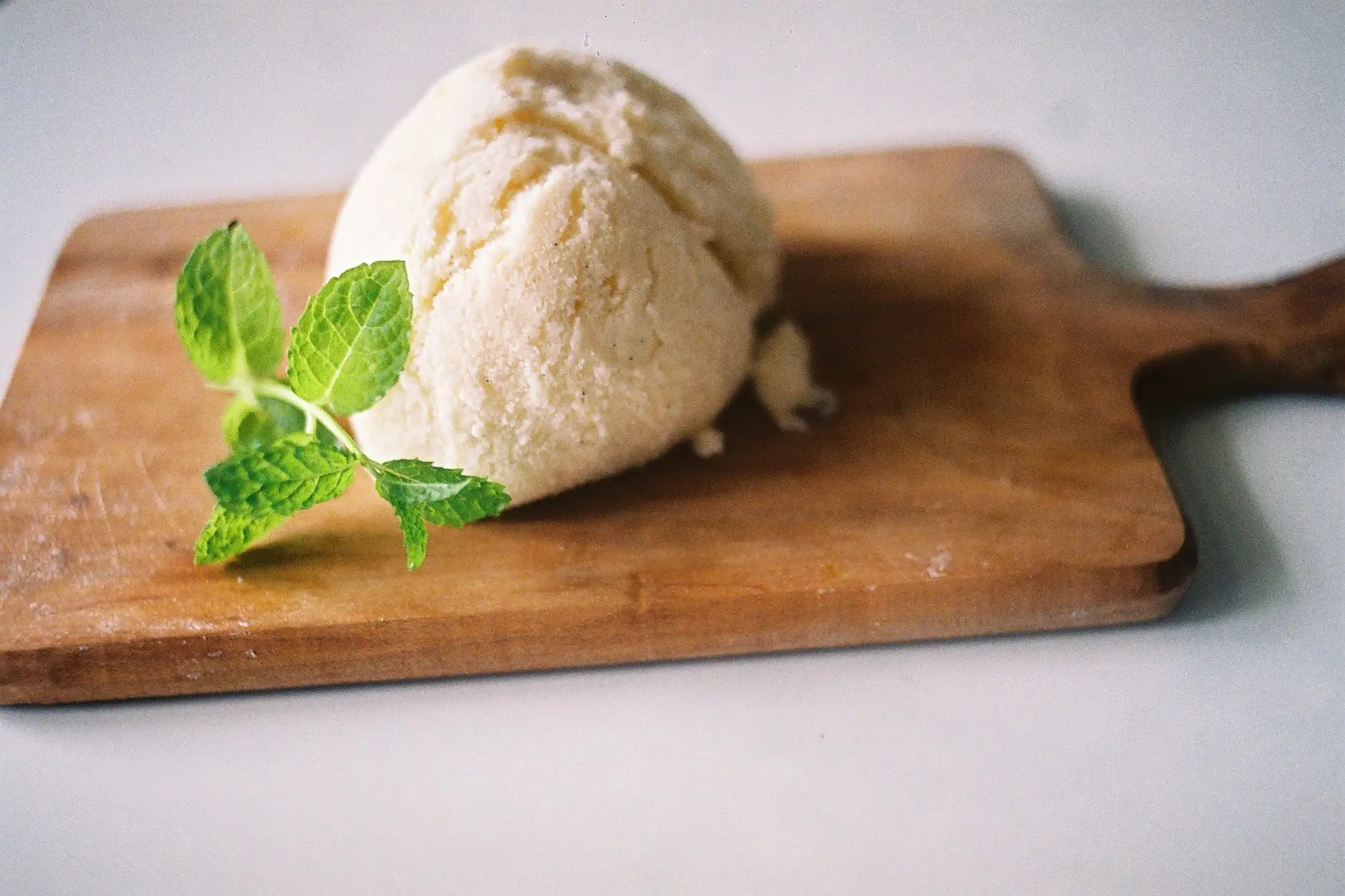 Boule de glace à la vanille posée sur une planche, avec une feuille de menthe.