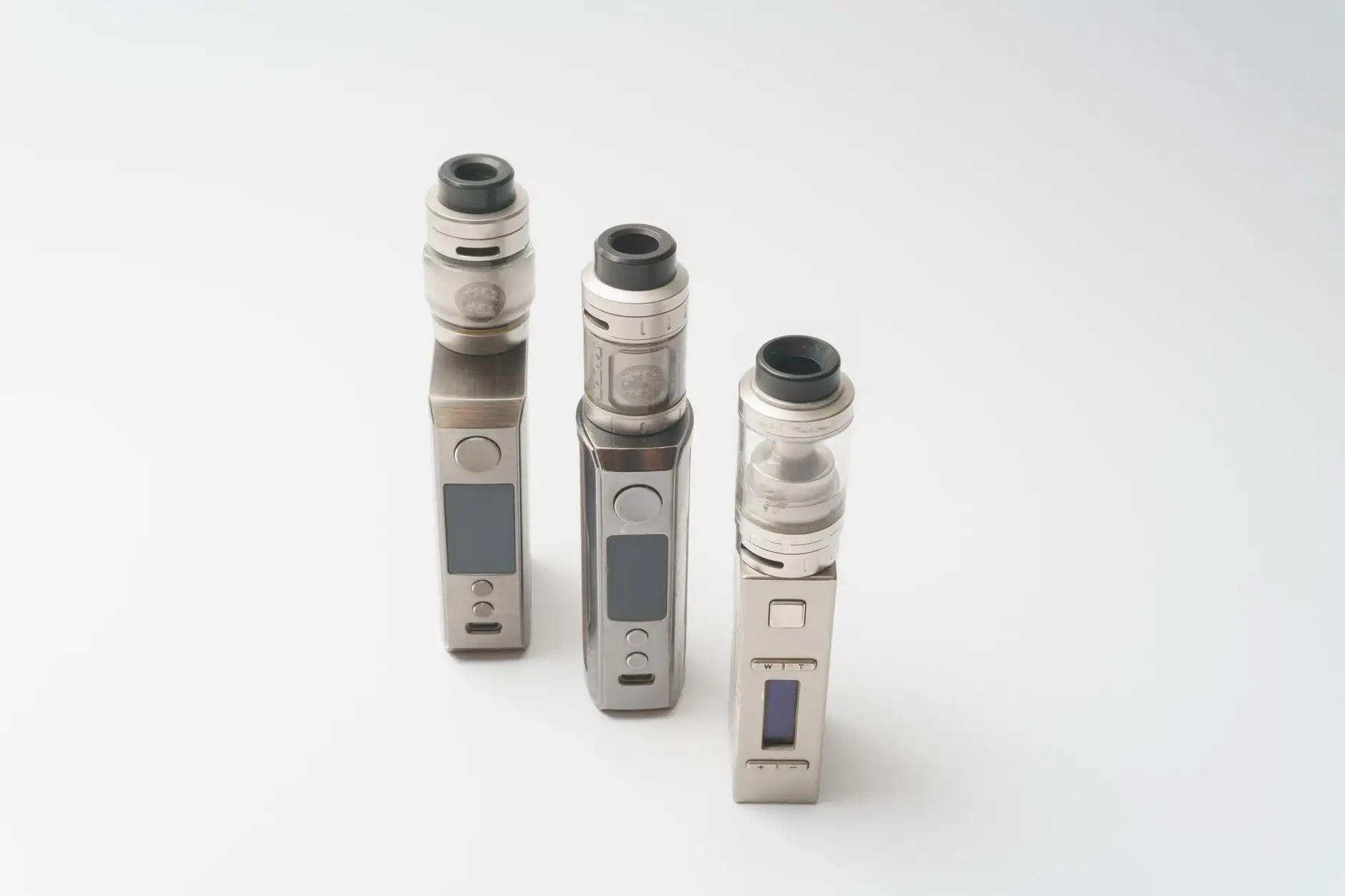 Trois cigarettes électroniques rechargeables à réservoir posées sur un fond blanc, le format qui reste autorisé