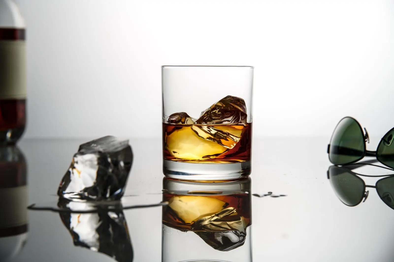 Verre de whisky sur glaçons posé sur une surface réfléchissante, fond blanc