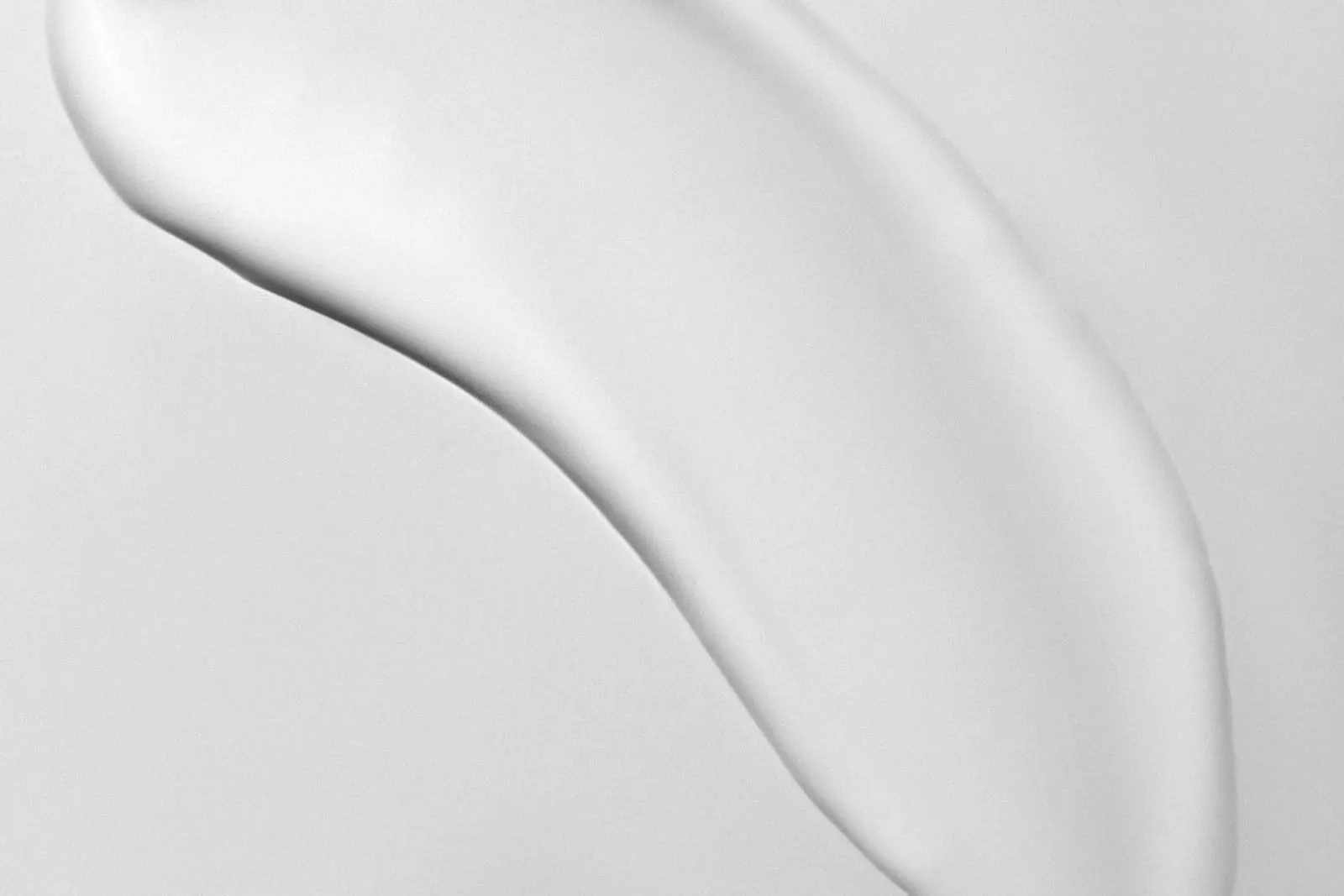 Trace de crème blanche étalée en courbe sur une surface blanche, vue de près