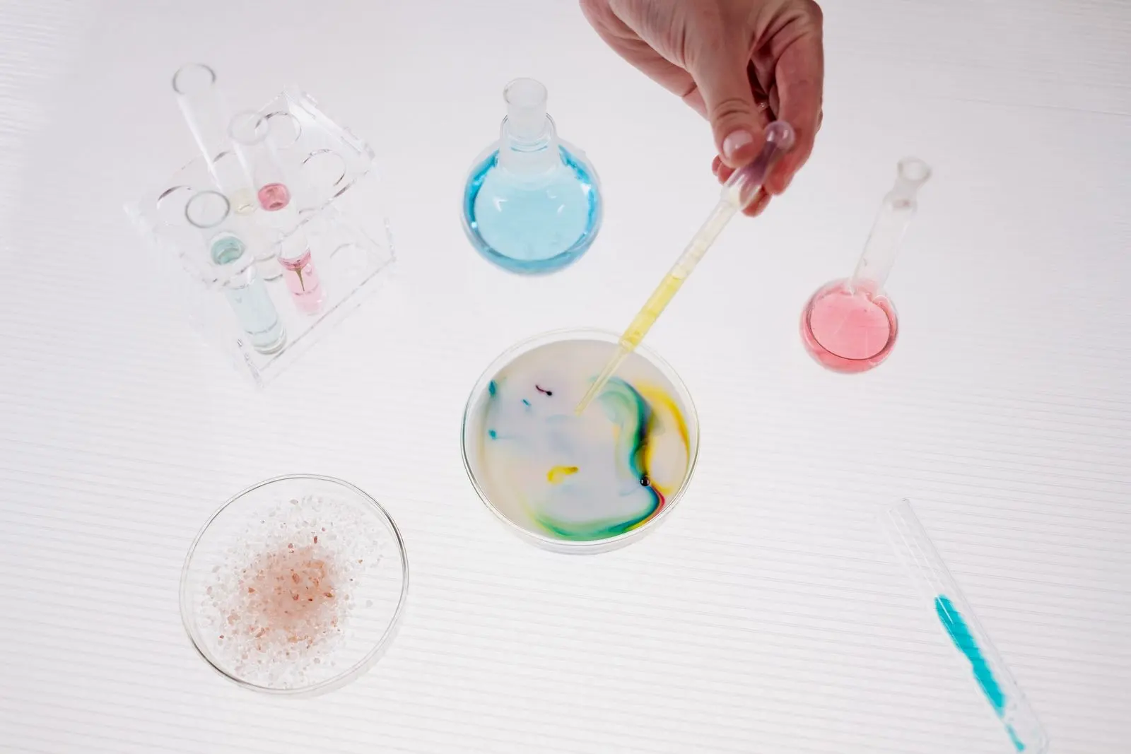 Pipette déposant un liquide dans une boîte de Petri remplie d'une émulsion blanche, entre flacons et tubes de laboratoire