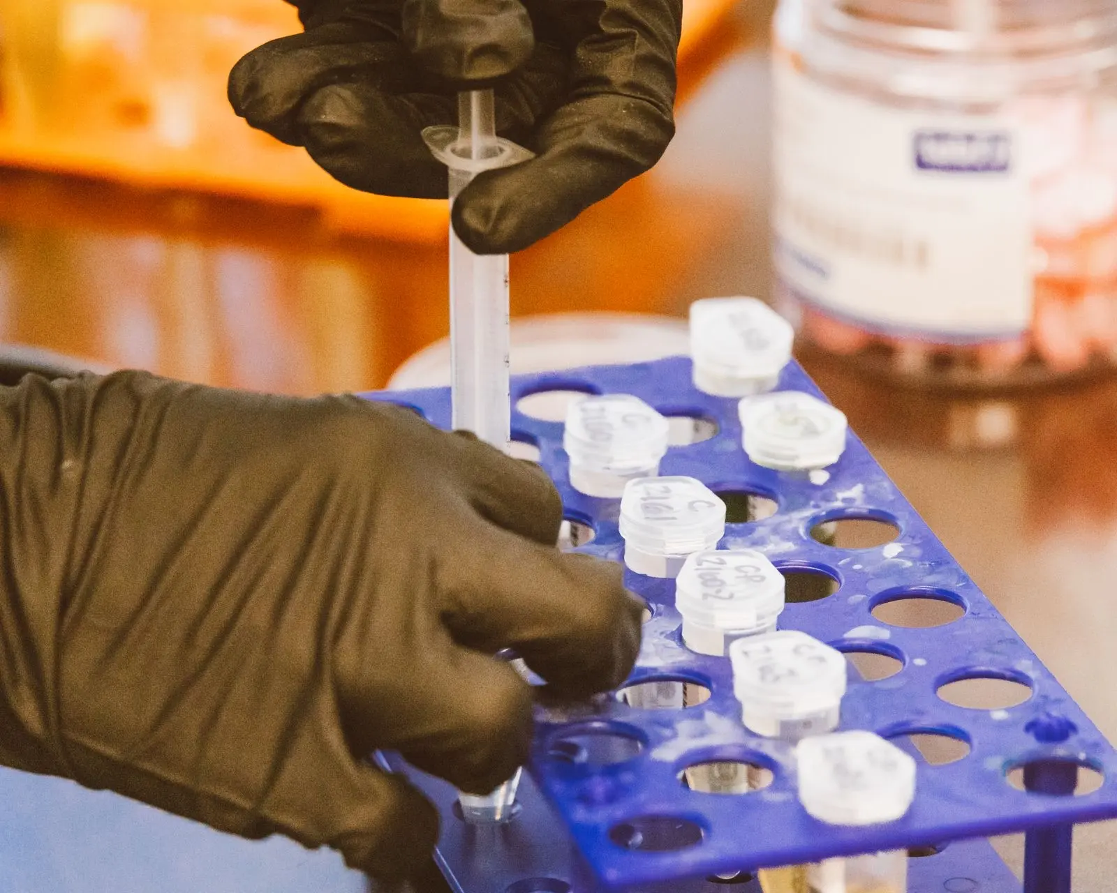 Mains gantées déposant des échantillons dans un portoir de laboratoire, étape de préparation avant une analyse chromatographique
