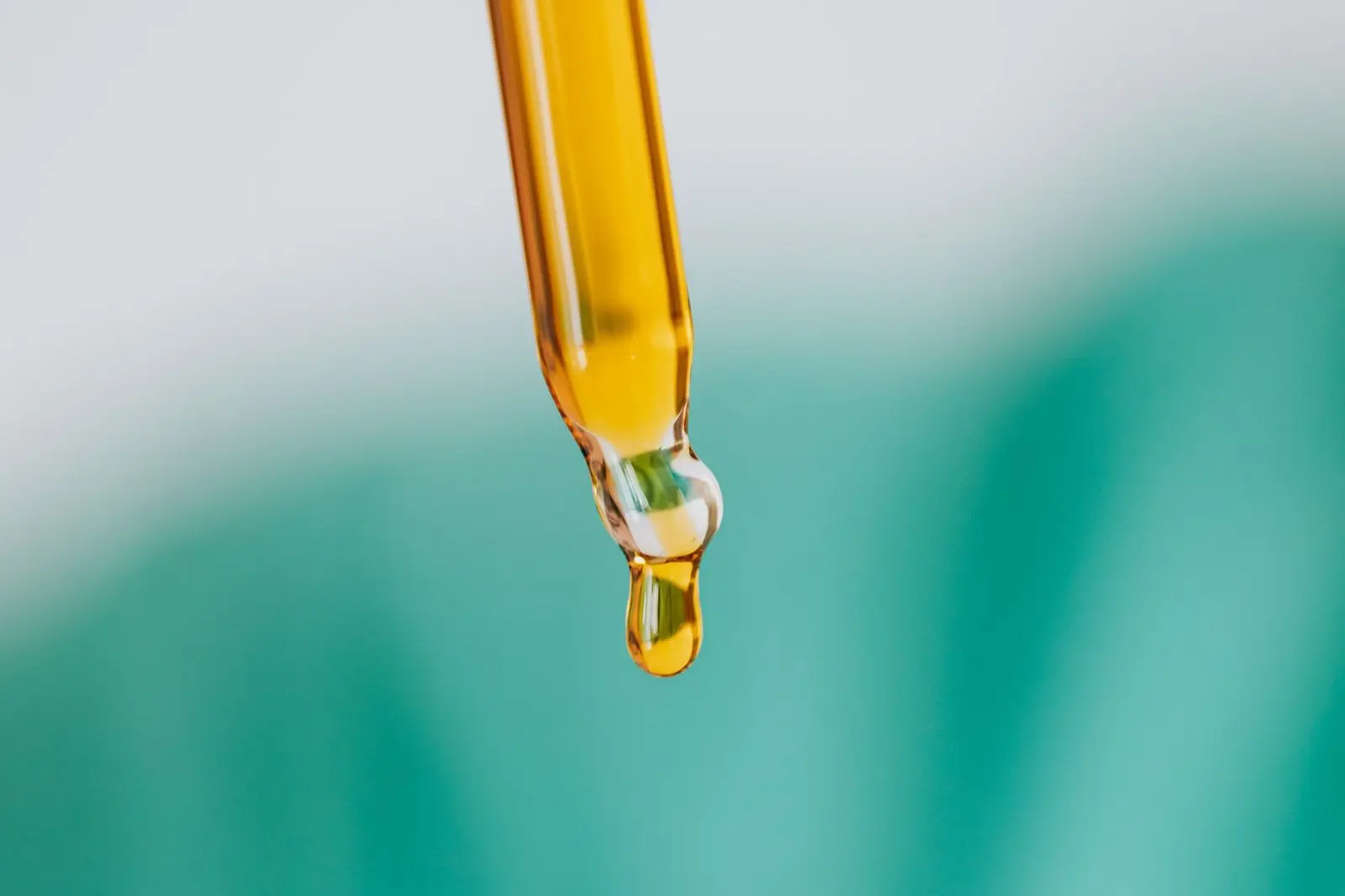 Pipette en verre laissant tomber une goutte d'huile ambrée, sur fond vert flou
