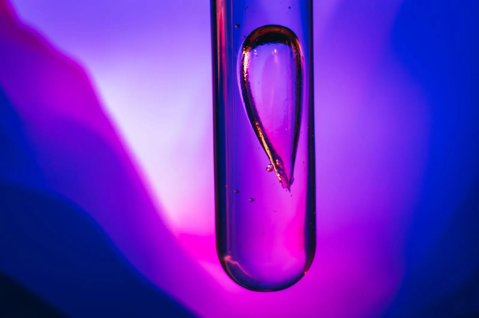 Goutte de liquide visqueux dans un tube à essai en verre, éclairée en violet