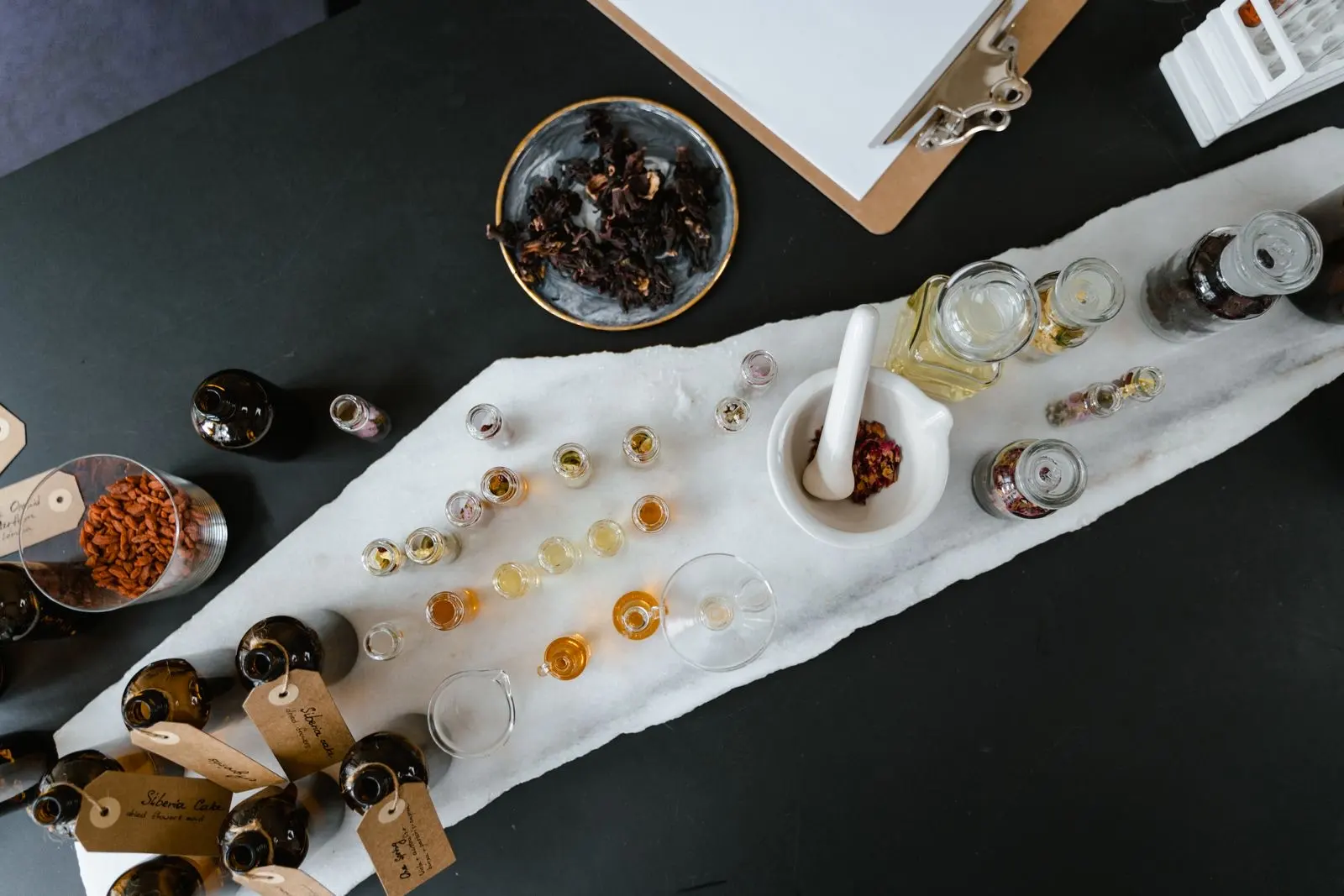 Flacons d'huiles en verre ambré et clair, pipettes et ingrédients végétaux posés sur une table, vus du dessus