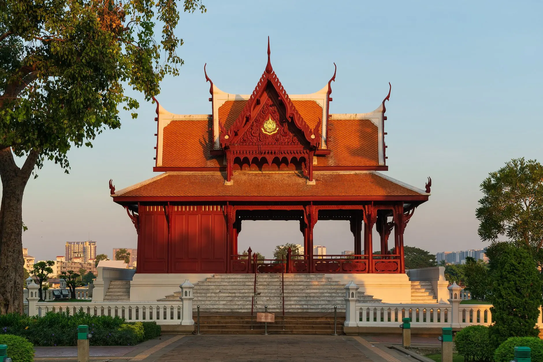 Pavillon de style thaï au toit rouge et or, sous un ciel clair.