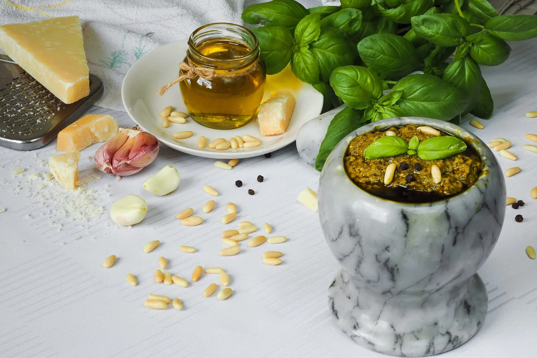 Pesto dans un mortier en marbre, entouré de basilic, parmesan, ail et pignons.