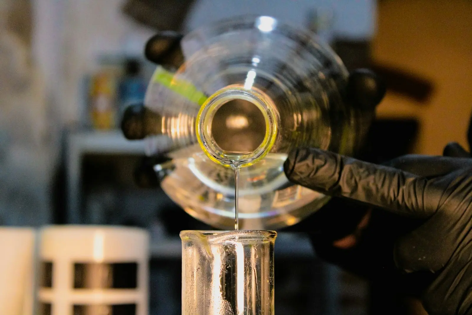 Main gantée versant un liquide dans un bécher, dans un laboratoire de chimie faiblement éclairé