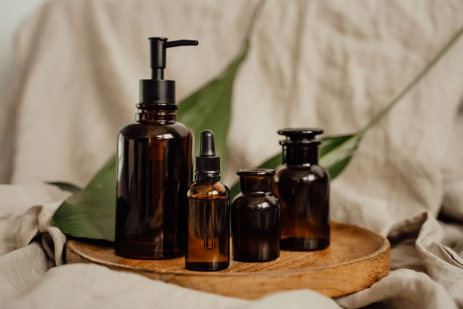 Flacons cosmétiques en verre ambré, dont un compte-gouttes et un flacon pompe, posés sur un plateau en bois