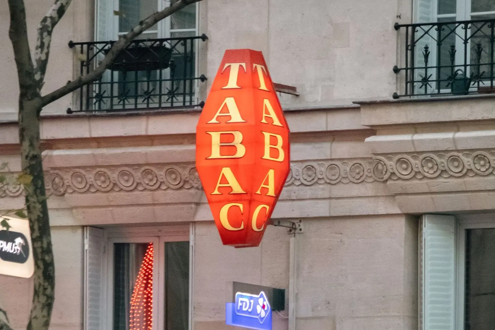 Enseigne rouge « Tabac » en losange sur la façade d'un immeuble parisien