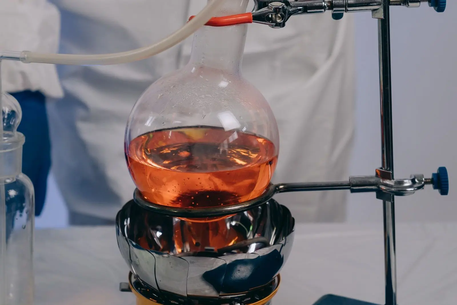 Ballon de laboratoire rempli d'un liquide orangé, posé sur un chauffe-ballon et maintenu par une pince