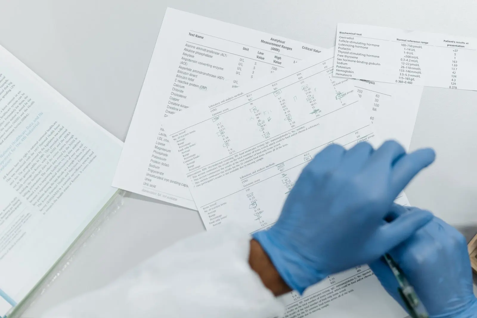 Mains gantées relisant des résultats d'analyse de laboratoire imprimés, tableaux de valeurs sur une table blanche