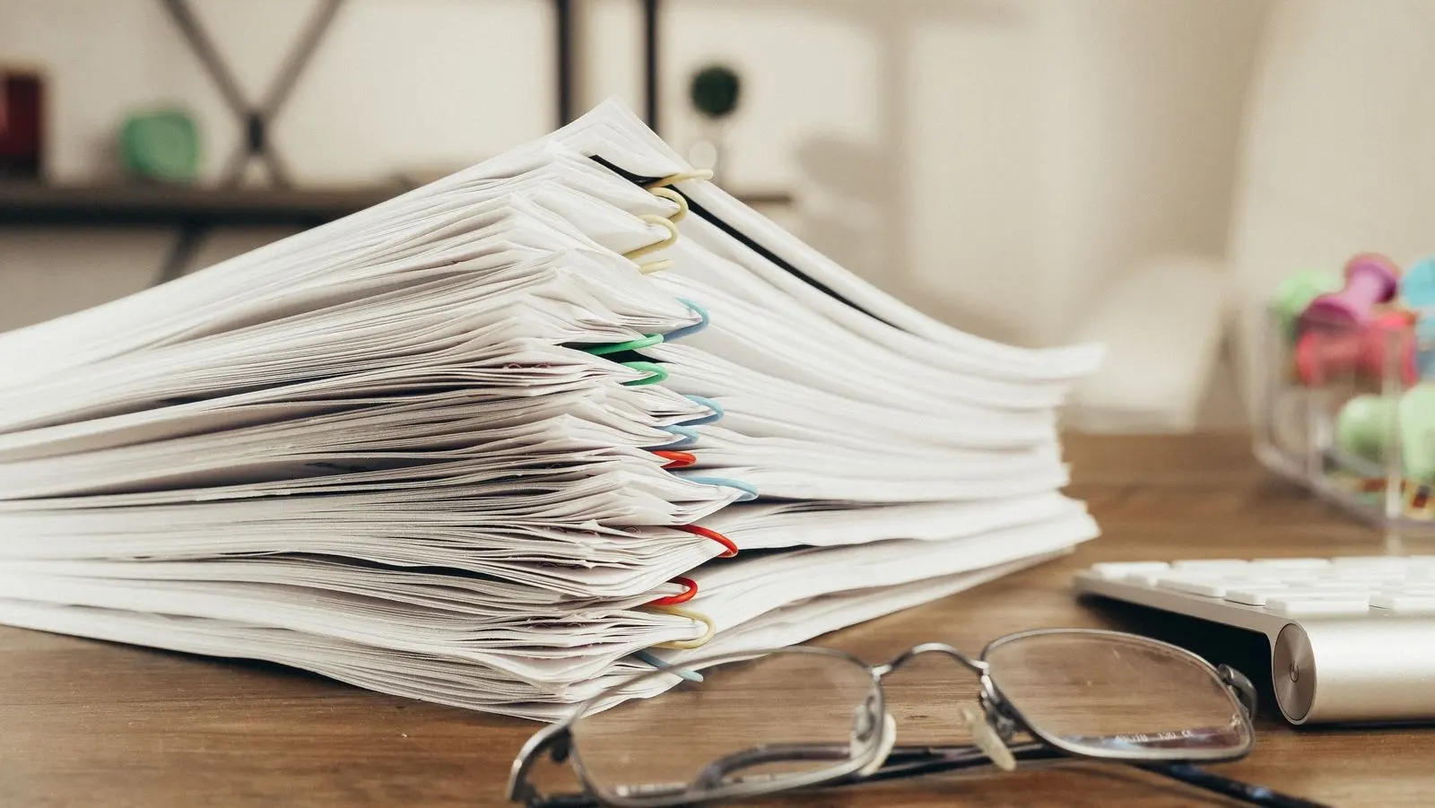 Pile de documents agrafés sur un bureau, à côté d'une paire de lunettes
