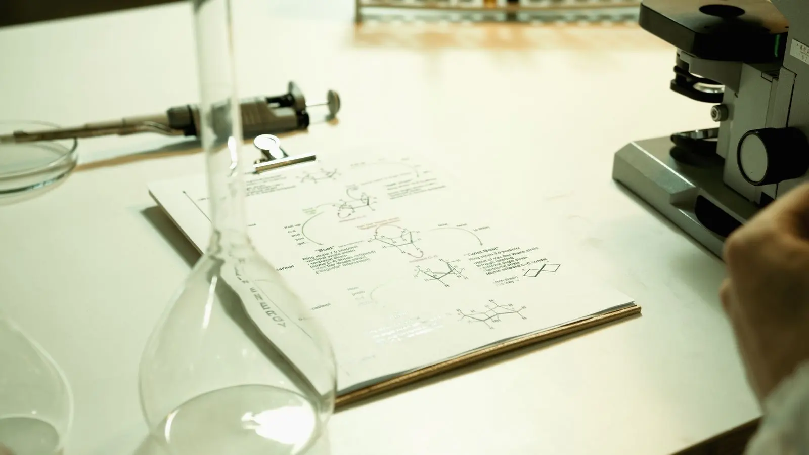 Paillasse de laboratoire avec une feuille de formules chimiques sur un porte-bloc, un flacon en verre et un microscope