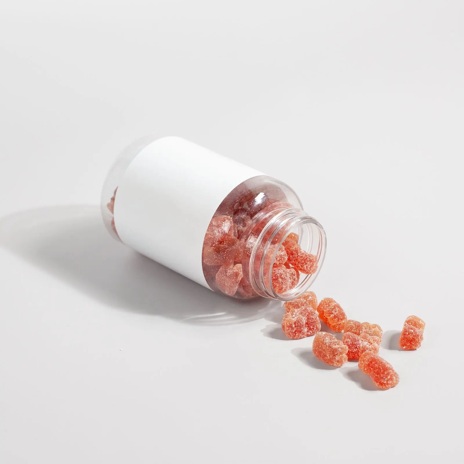 Pot sans étiquette renversé sur une table blanche, laissant échapper des gommes rouges sucrées