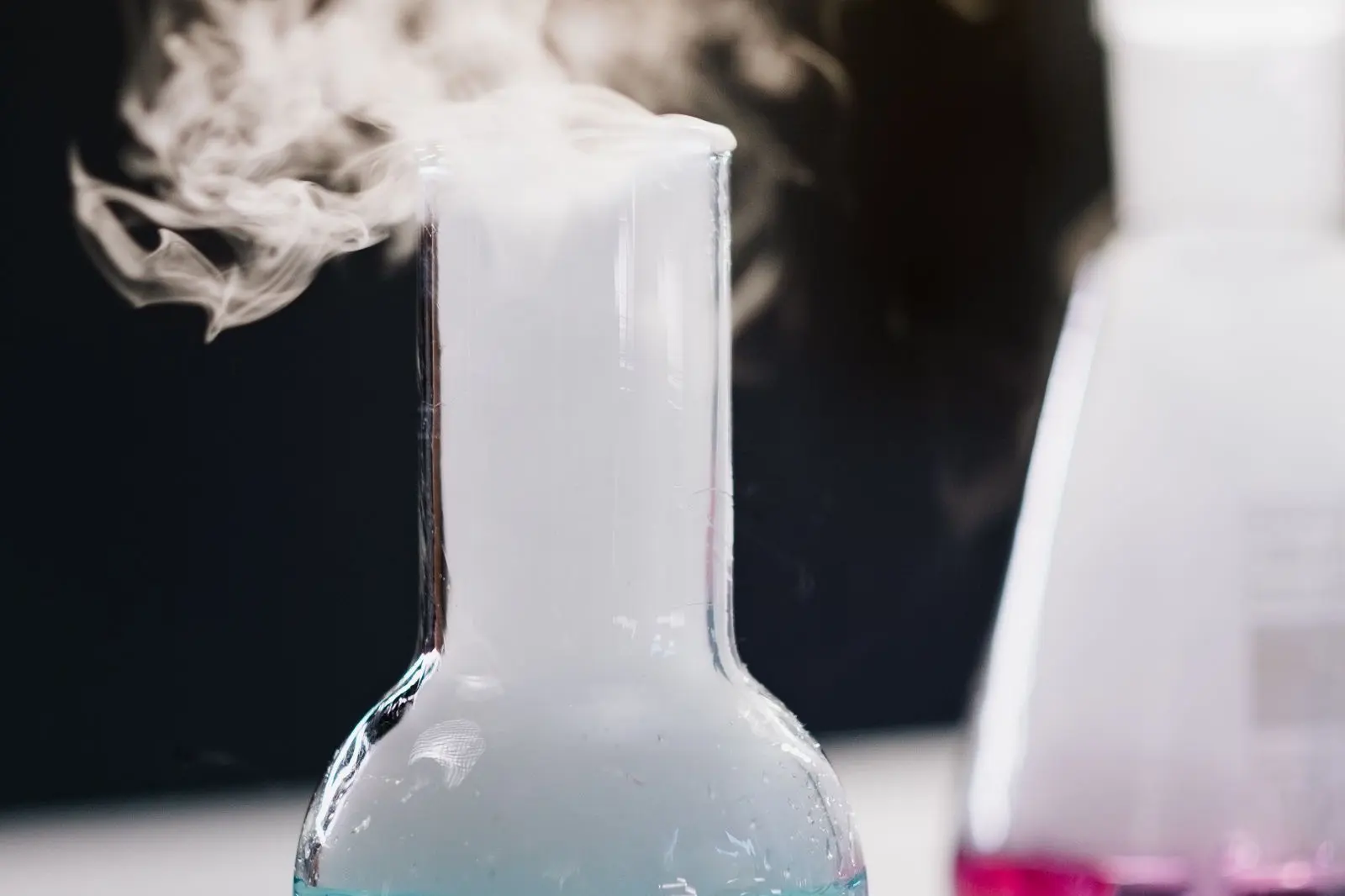 Ballon de laboratoire d'où s'échappe une vapeur blanche, sur fond sombre