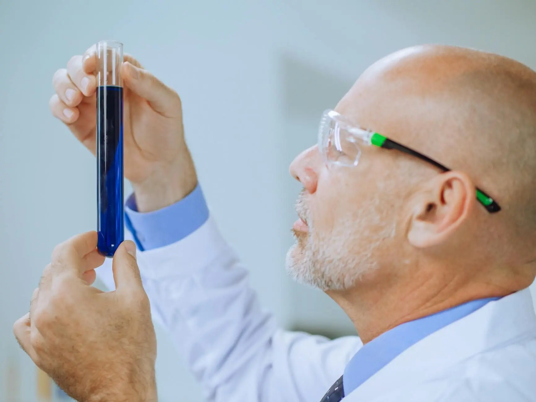 Une personne en blouse et lunettes examine un tube contenant un liquide bleu dans une photographie d'illustration.